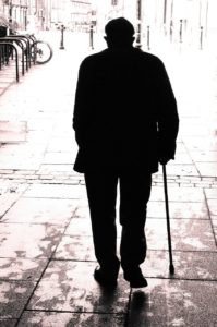 old black man with cane walking away in shadows